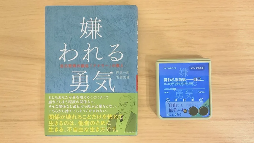 机の上に並べた岸見一郎・古賀史健『嫌われる勇気』の紙の本と、Audibleの再生画面を映したスマートフォン